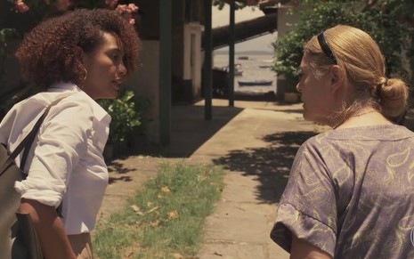 As atrizes Taís Araujo e Magali Biff conversam enquanto adentram o quintal de uma casa em cena da novela Amor de Mãe