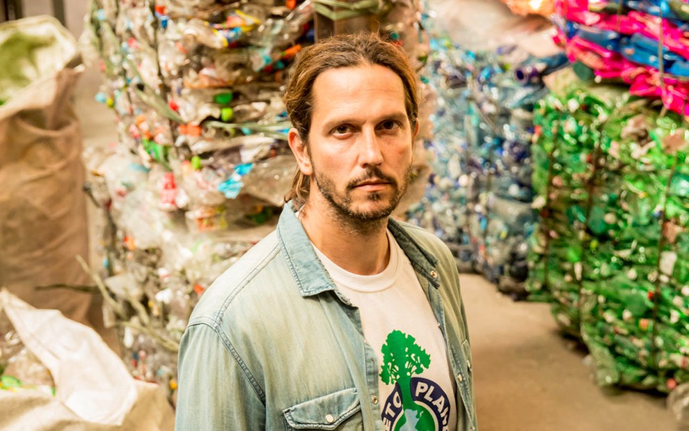 O ator Vladimir Brichta caracterizado como o personagem Davi diante de vários fardos de lixo reciclável em um galpão na cidade cenográfica de Amor de Mãe nos Estúdios Globo, no Rio