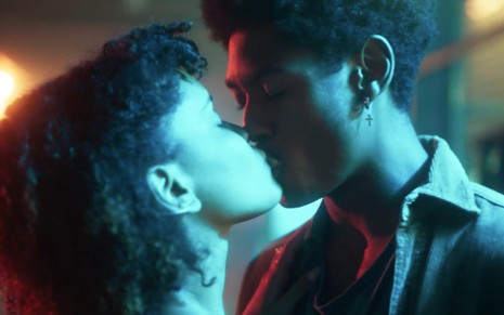 Heslaine Vieira e Matheus Campos em cena de As Five: cobertos por luzes azuladas, casal se beija