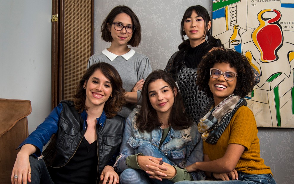 Daphne Bozaski (Benê) e Ana Hikari (Tina) em pé, Manoela Aliperti (Lica), Gabriela Medvedovski (Keyla) e Heslaine Vieira (Ellen) sentadas em um sofá em cena de Viva a Diferença