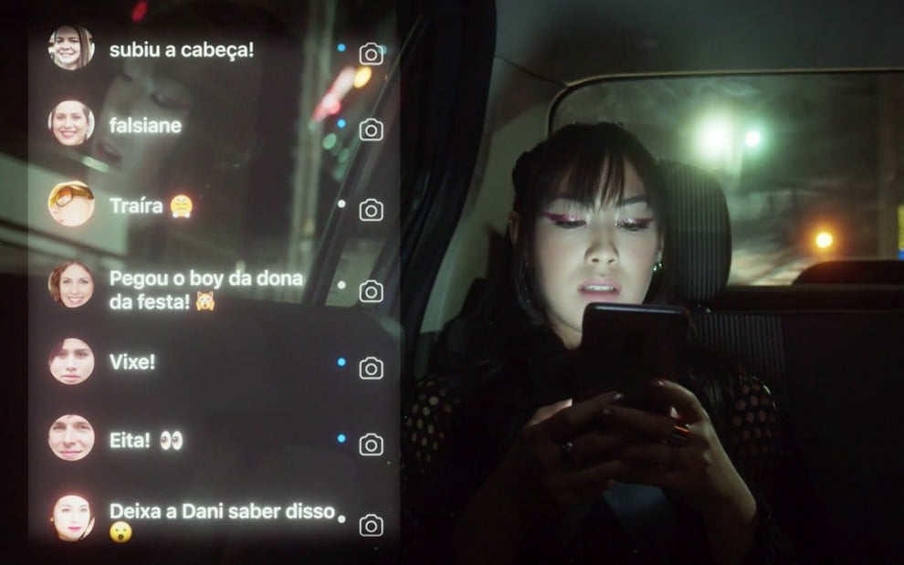 Ana Hikari em cena de As Five: caracterizada como Tina, personagem olha para a tela do celular cheia de comentários odiosos sobre ela