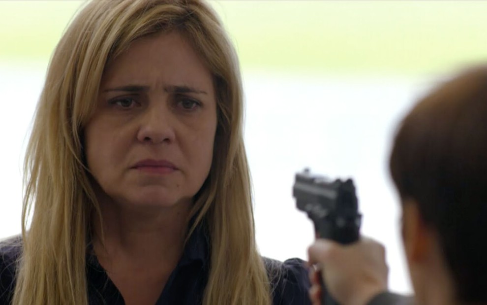A atriz Adriana Esteves, com expressão de resignação, na mira de um revólver caracterizada como a Carminha em Avenida Brasil