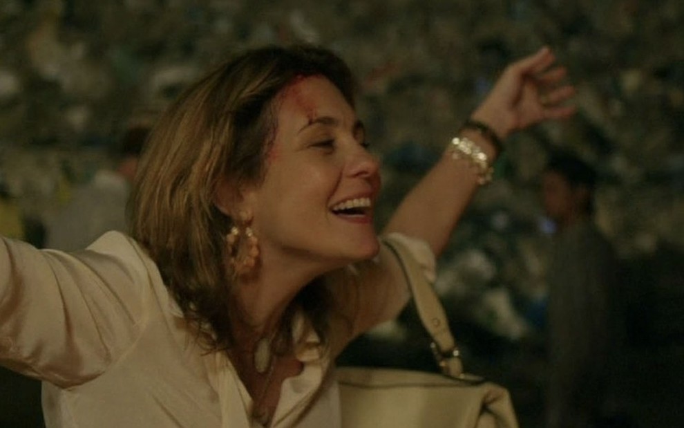 A atriz Adriana Esteves de braços abertos e machucados no rosto caracterizada como a Carminha de Avenida Brasil