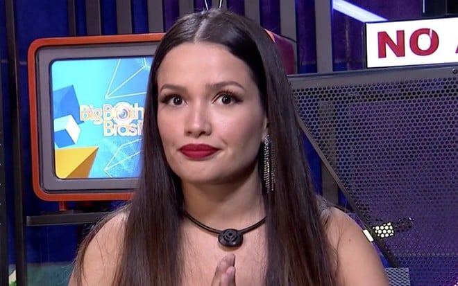 Juliette Freire com cabelo alisado e de batom vermelho com as duas mãos juntas dentro do confessionário do BBB21