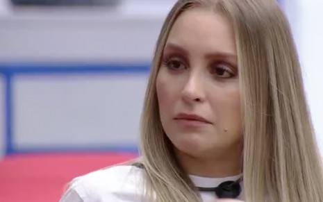 A atriz Carla Diaz com expressão de tristeza sentada em um sofá na área externa do Big Brother Brasil