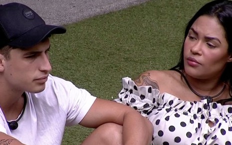 Os ex-participantes do BBB20 Felipe Prior (à esquerda) e Flayslane Raiane (à direita) conversando durante o reality da Globo, sentados em um gramado