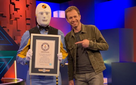 O apresentador Tiago Leifert posa ao lado de um homem fantasiado que segura um certificado do Guinness World Records