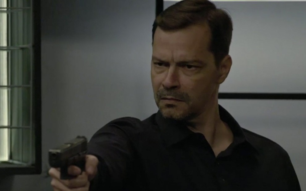 Heitor Martinez em cena de Amor Sem Igual: caracterizado como Bernardo, personagem usa camisa preta e aponta arma para alguém fora do quadro