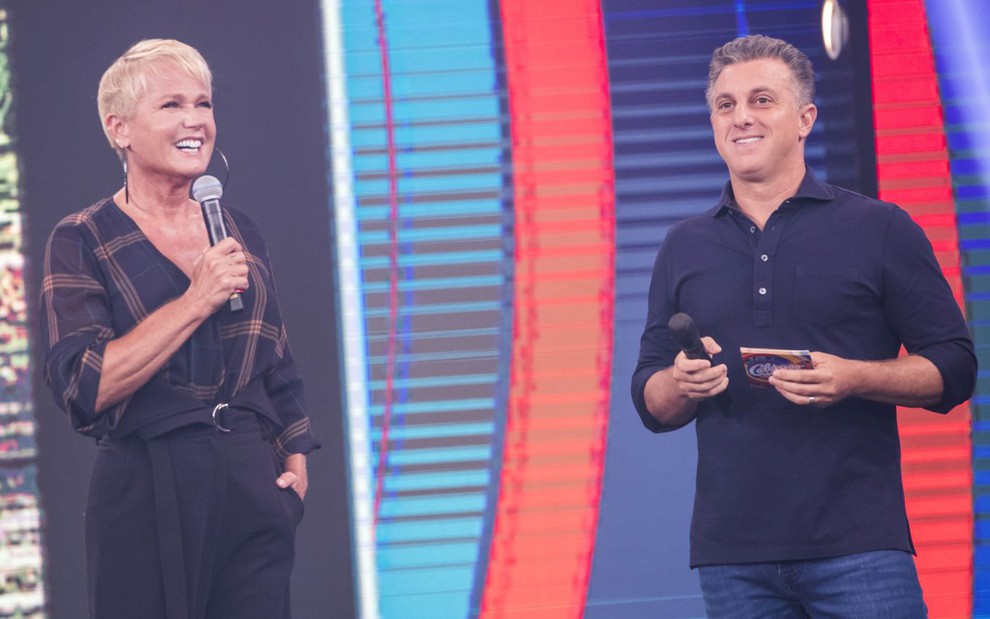 Xuxa e Luciano Huck no palco do Caldeirão, ambos de roupa escura