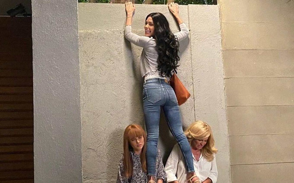 As atrizes Juliana Paiva, Vitória Strada e Deborah Secco, usando peruca, prestes a pular um muro, em cena como Luna, Kyra e Alexia em Salve-se Quem Puder
