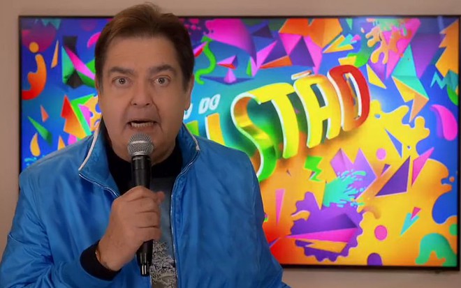 Fausto Silva à frente de painel com o logotipo do Domingão do Faustão instalado em sua casa, em São Paulo