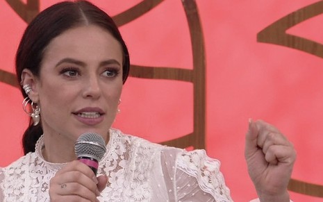 A atriz Paolla Oliveira segura um microfone em frente a um cenário rosa no Escontro