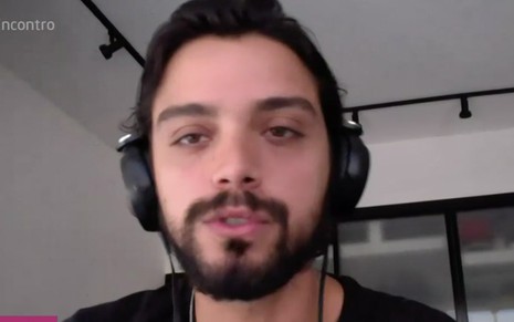 O ator Rodrigo Simas com um fone de ouvido do tipo headseat preto em um escritório durante uma chamada de vídeo ao Encontro