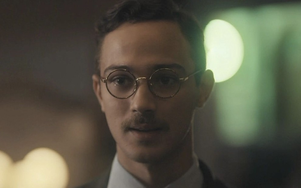 O ator André Luiz Frambach, com um óculos de armação redonda e um bigode, caracterizado como o Julinho em cena de Éramos seis