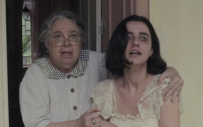 Camila Amado, à esquerda como Candoca, segura Júlia Stockler, a Justina, com expressão aterrorizada em cena de Éramos Seis
