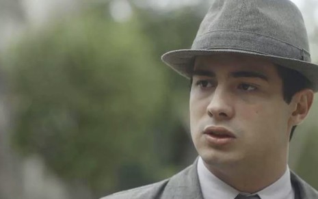 O ator Danilo Mesquita, com um terno e um chapéu cinza, caracterizado como o Carlos em cena de Éramos Seis