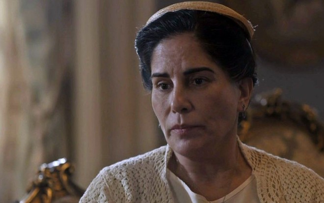A atriz Gloria Pires com uma boina e um vestido de tricô creme caracterizada como a personagem Lola em cena de Éramos Seis, ela tem a expressão desolada