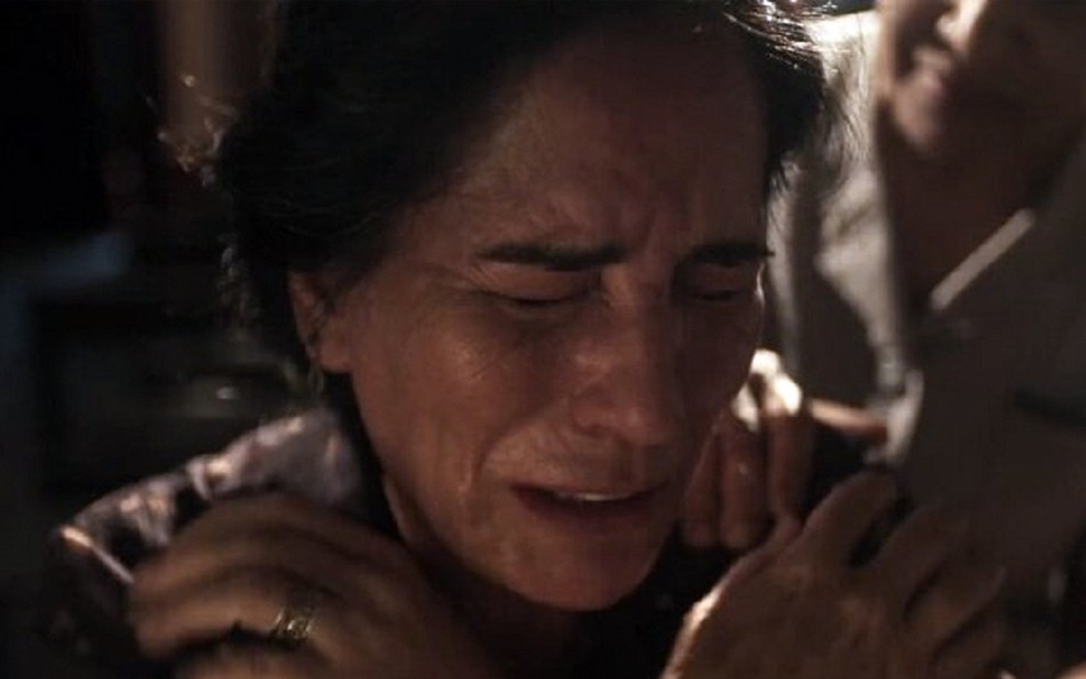 Em close up, a atriz Gloria Pires está chorando, abraçada aos seus ombros, caracterizada como a Lola em Éramos Seis