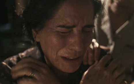 A atriz Gloria Pires, em close-up, com as mãos sobre o peito e expressão de choro, caracterizada como a Lola em cena de Éramos Seis