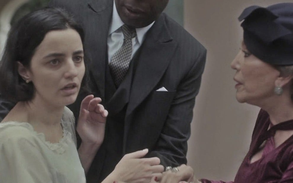 A atriz Julia Stockler tenta fugir nos braços de um homem de paletó enquanto é observada por Susana Vieira, a Emília, em cena de Éramos Seis
