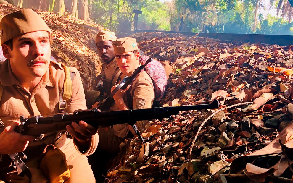 Os atores Nicolas Prattes, Jhona Burjack e Izak Dahora vestidos de soldados com armas nas mãos em cena de Éramos Seis