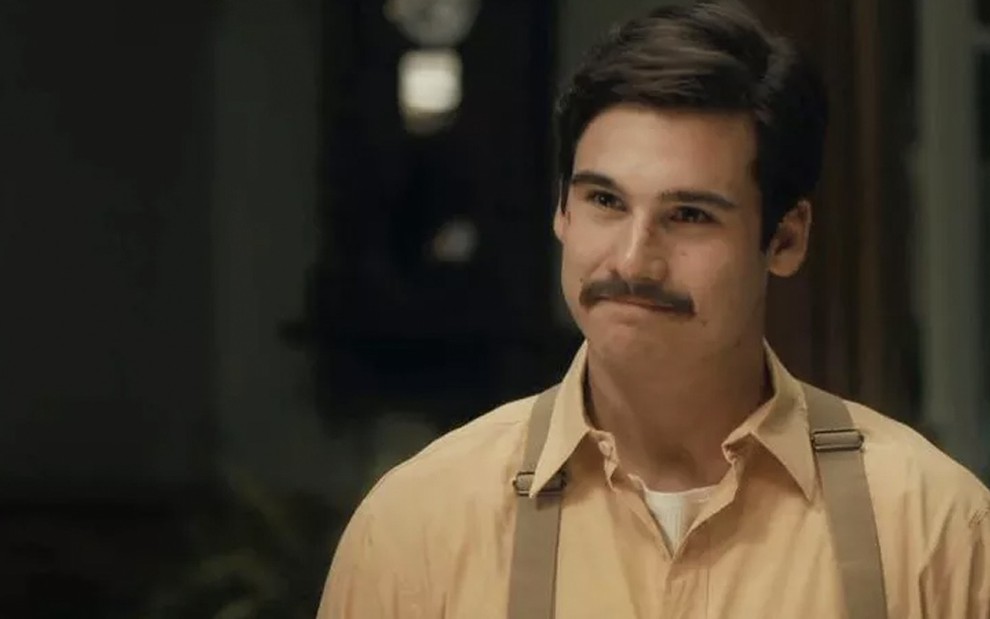 O ator Nicolas Chaves, de blusa bege e suspensório, sorri de bigodes, caracterizado como o Alfredo em cena de Éramos Seis