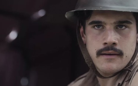 O ator Nicolas Prattes, em close up, usa uma farda cáqui e um capacete preto, caracterizado como Alfredo em cena de Éramos Seis