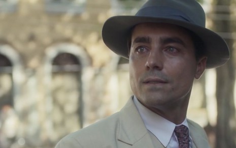 O ator Ricardo Pereira olha para o lado esquerdo com terno e chapéu caracterizado como o Almeida em cena de Éramos Seis