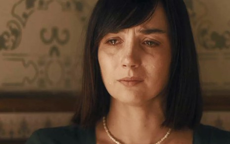 A atriz Simone Spoladore, com um vestido verde, cordão dourado e os olhos cheios de lágrimas, caracterizada como a Clotilde em cena de Éramos Seis
