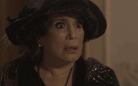 A atriz Susana Vieira, com um chapéu e vestido pretos, caracterizada como a Emília em cena de Éramos Seis