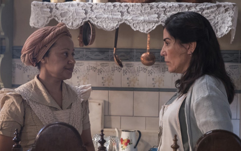 A atriz Virgínia Rosa à esquerda, a Durvalina, olha para Gloria Pires à direita, como a Lola, em uma cena na cozinha da casa de Lola em Éramos Seis