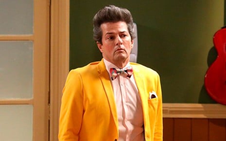 Marcelo Serrado caracterizado como Crô na Escolinha do Professor Raimundo: ator usa terno amarelo, camisa rosa clara e gravata borboleta estampada