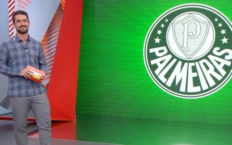 Felipe Andreoli no estúdio do Globo Esporte SP, ao lado de um telão com o escudo do Palmeiras