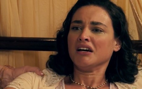 A atriz Débora Nascimento deitada em uma casa, com suor no rosto e expressão de desespero caracterizada como a Filomena em cena de Êta Mundo Bom!