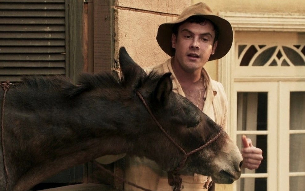 Caracterizado como Candinho, o ator Sergio Guizé conversa com um burro em cena de Êta Mundo Bom!