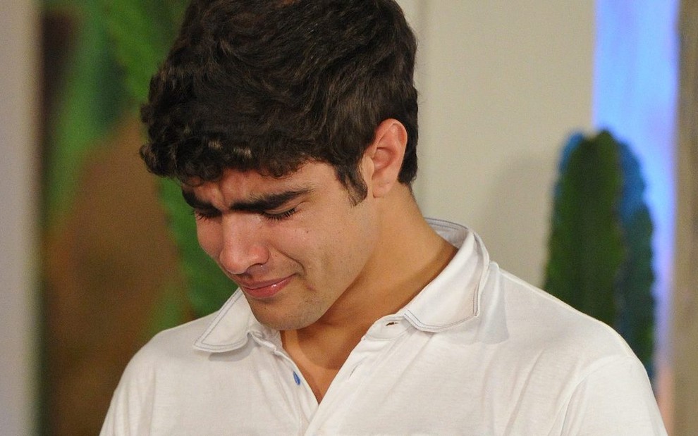 O ator Caio Castro usa camiseta branca e chora com a cabeça baixa em gravação da novela Fina Estampa, da TV Globo