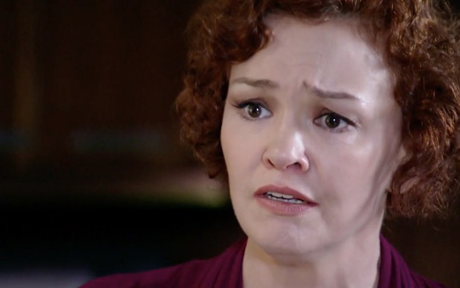 Julia Lemmertz caracterizada como Esther em Fina Estampa; personagem tem o olhar triste e usa blusa na cor bordô