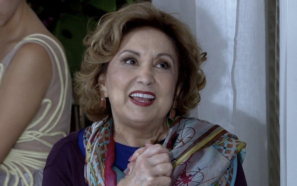 A atriz Eva Wilma, usando um xale, e com expressão feliz, como íris na novela Fina Estampa