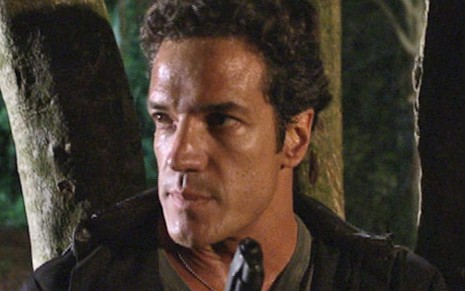 O atro Carlos Machado segura um revólver próximo ao rosto e aprontado para cima em cena da novela Fina Estampa