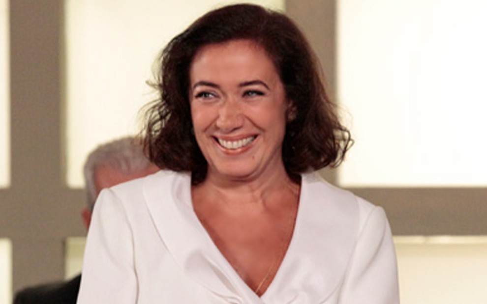 Lilia Cabral caracterizada como Griselda em Fina Estampa: personagem usa blazer branco e sorri para alguém fora do quadro