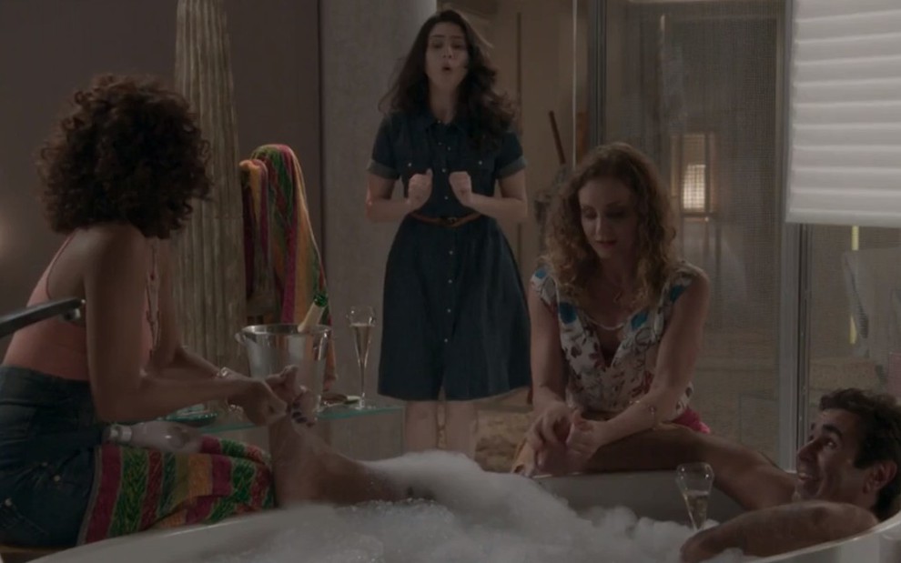 Orã Figueiredo dentro de uma banheira em cena como Hugo; Olivia Torres (Débora) ao fundo espantada ao ver o pai com duas mulheres na novela Totalmente Demais