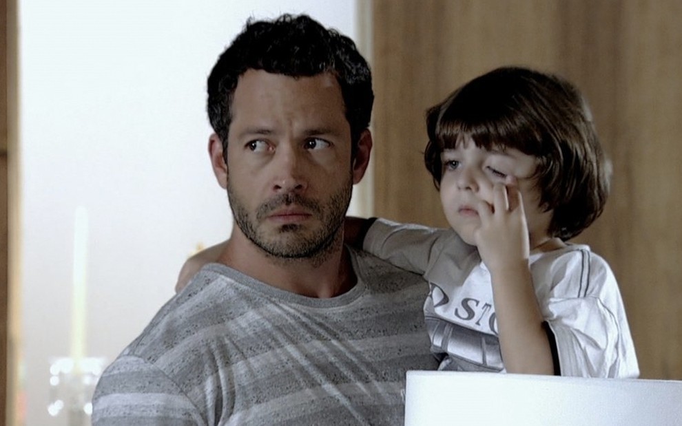 O ator Malvino Salvador caracterizado como Quinzé carrega o ator Gabriel Pelícia no colo como o Quinzinho, o menino coça os olhos, em cena de Fina Estampa