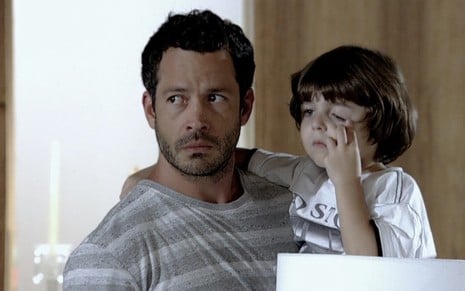 O ator Malvino Salvador caracterizado como Quinzé carrega o ator Gabriel Pelícia no colo como o Quinzinho, o menino coça os olhos, em cena de Fina Estampa