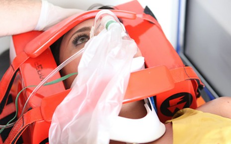 A atriz Suzana Pires deitada em maca, com respirador e colar cervical, em cena de resgate médico de Fina Estampa