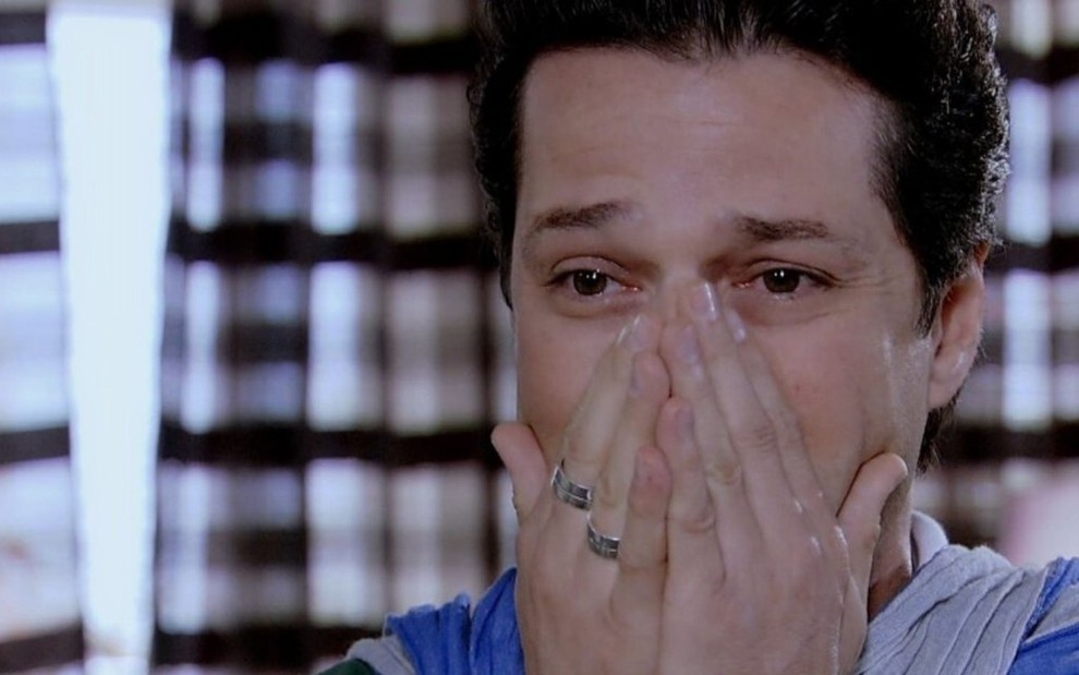 O ator Marcelo Serrado, com expressão assustada e de choro, com as mãos na boca, em cena como Crô em Fina Estampa
