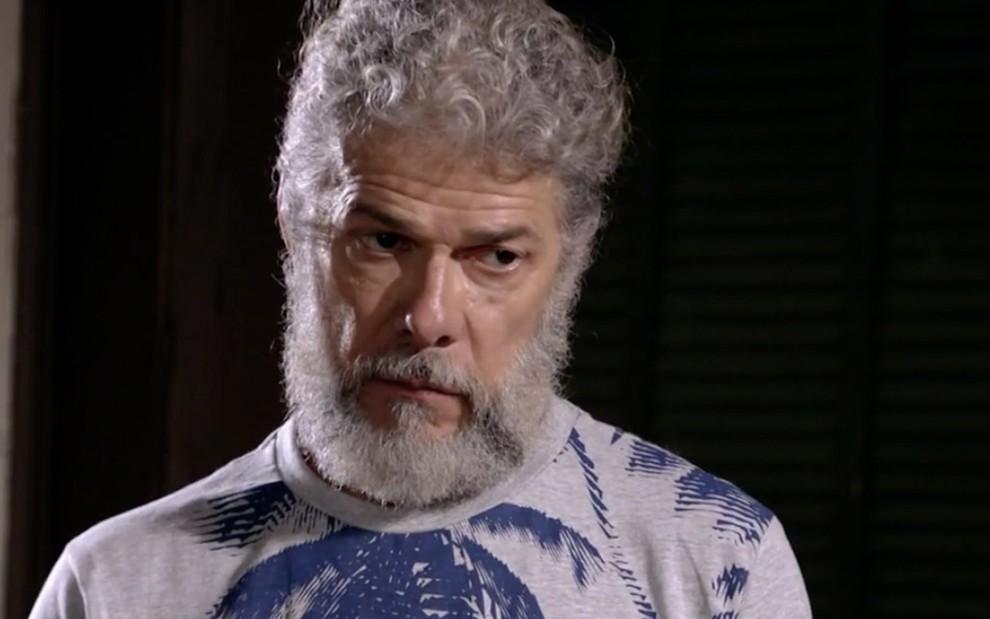 José Mayer caracterizado como o personagem Pereirinha, de Fina Estampa: ator usa camiseta estampa com palmeiras azul e está com o cabelo grande e barba espessa