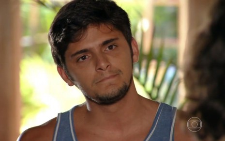O ator Bruno Gissoni, usando uma camiseta regata azul, com expressão séria, em cena como Juliano na novela Flor do Caribe