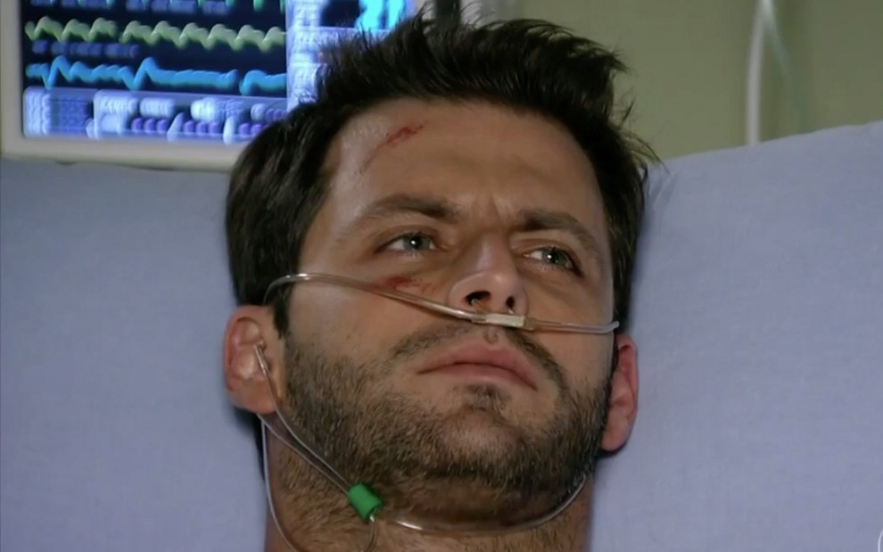 Henri Castelli em cena de Flor do Caribe: caracterizado como Cassiano, ator está em uma maca de hospital e usa tubo de respiração