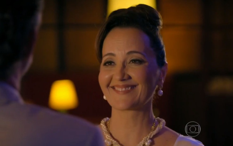 A atriz Claudia Netto, com expressão de satisfação e sorriso no rosto, em cena como Guiomar, em Flor do Caribe