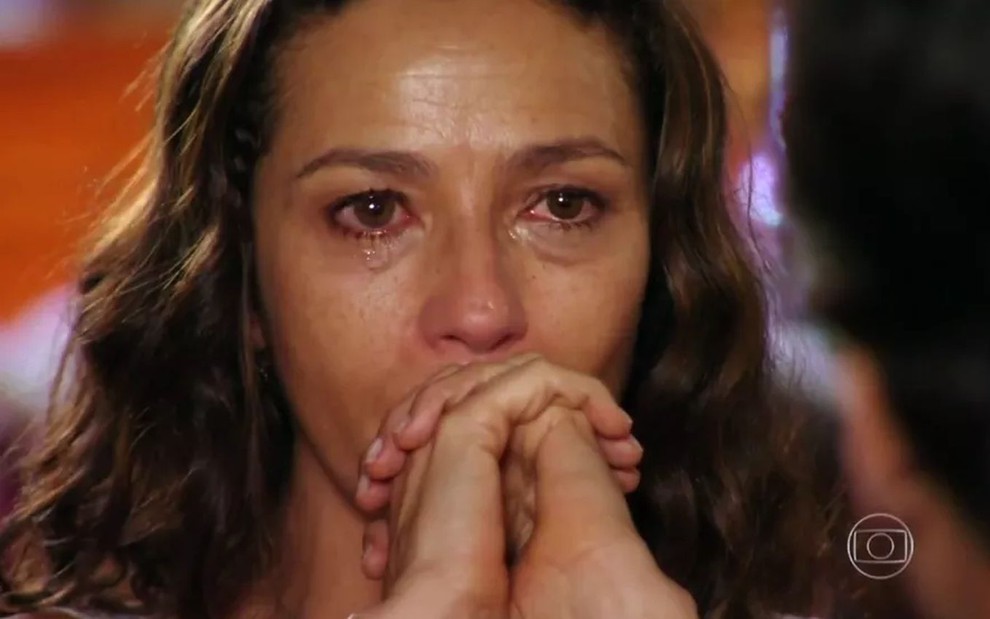 Bibiana (Cyria Coentro) chora com as mãos com os dedos cruzados na altura da boca em cena de Flor do Caribe